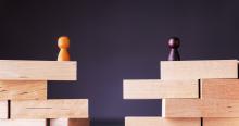 Two wooden block structures with separated pawn figures, symbolizing organizational division, cultural distance, or merger integration challenges.